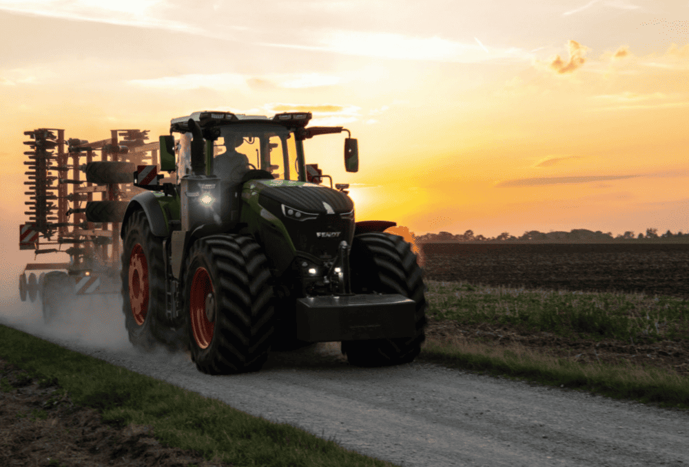 Un tractor fumiga un campo al atardecer, levantando polvo en un camino rural.