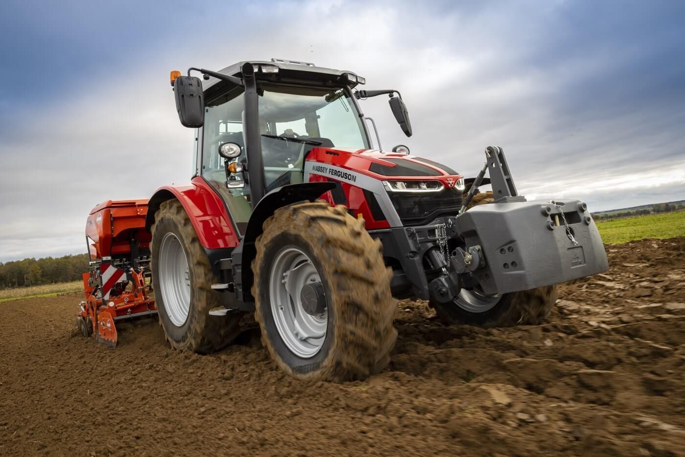 Tractor rojo con contrapeso delantero y cultivador trasero circulando por un campo embarrado bajo un cielo nublado.