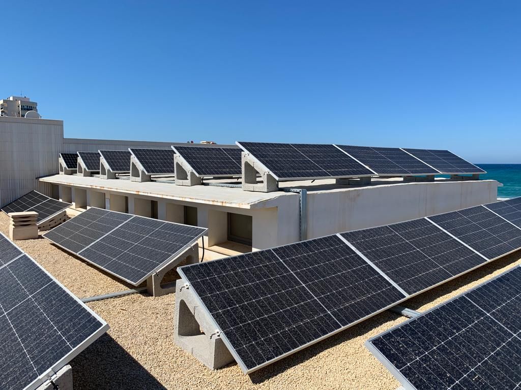 Una fila de paneles solares en el tejado de un edificio al lado del océano.