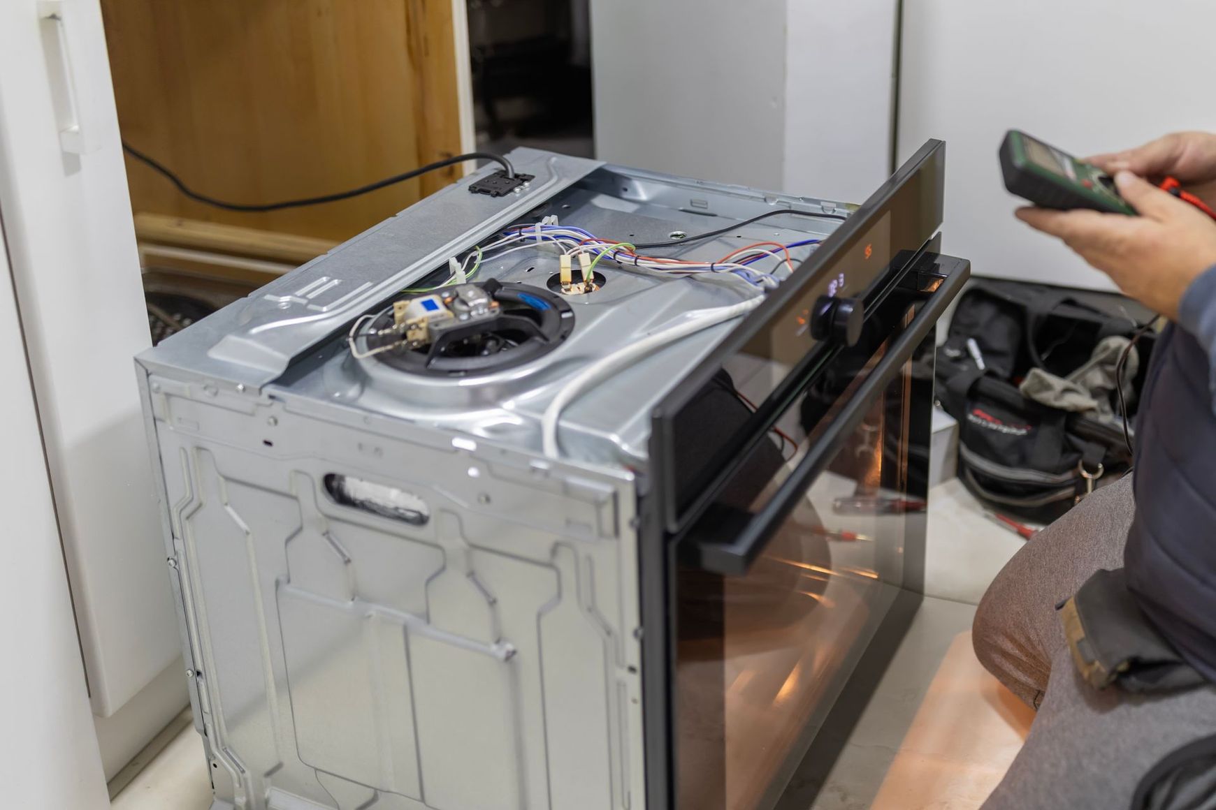 Un technicien utilise un multimètre pour inspecter le câblage et les composants d'un four dont le couvercle supérieur a été retiré.