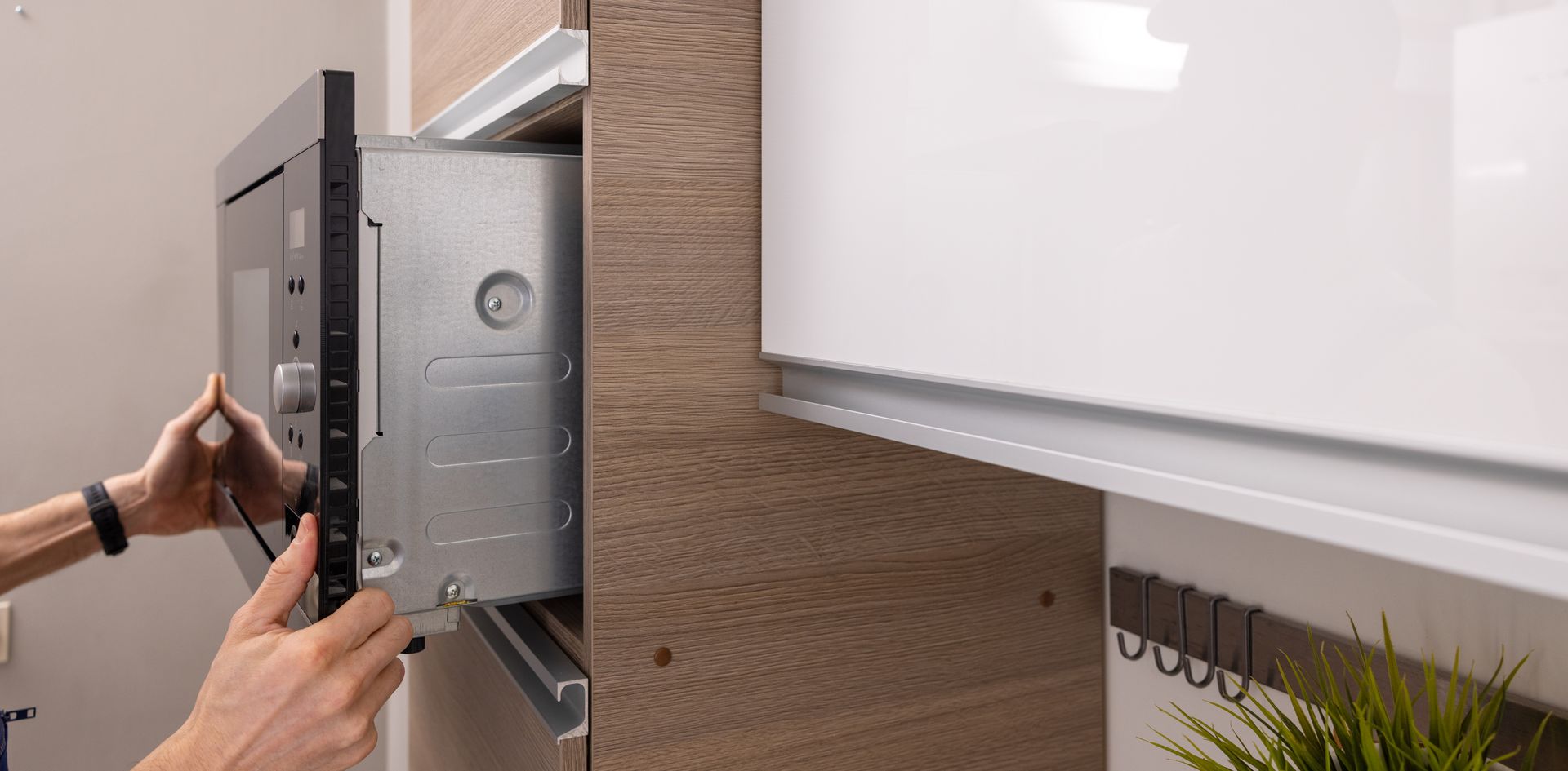 Les mains d'une personne glissent un four à micro-ondes encastrable métallique dans l'ouverture d'un placard de cuisine en bois.