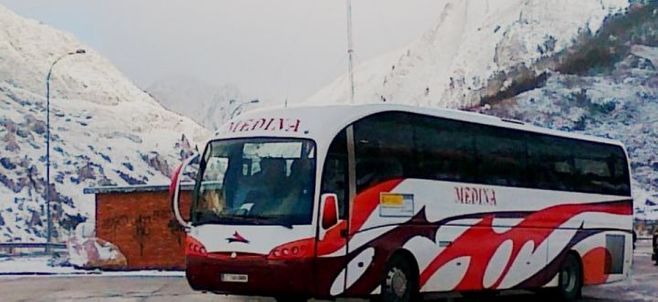 Un autobús rojo y blanco está estacionado frente a una montaña nevada.
