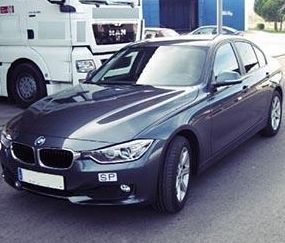 Un BMW negro está estacionado al costado de la carretera al lado de un camión blanco.