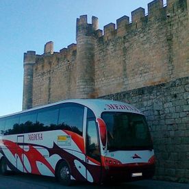 Un autobús rojo y blanco está estacionado frente a un muro de piedra.
