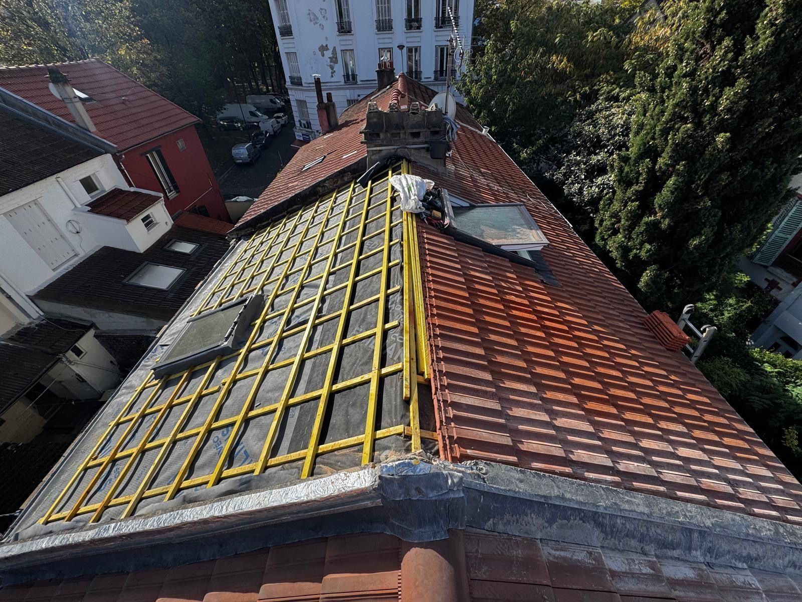 Toiture en tuiles rouges partiellement construite, avec charpente en bois apparente.