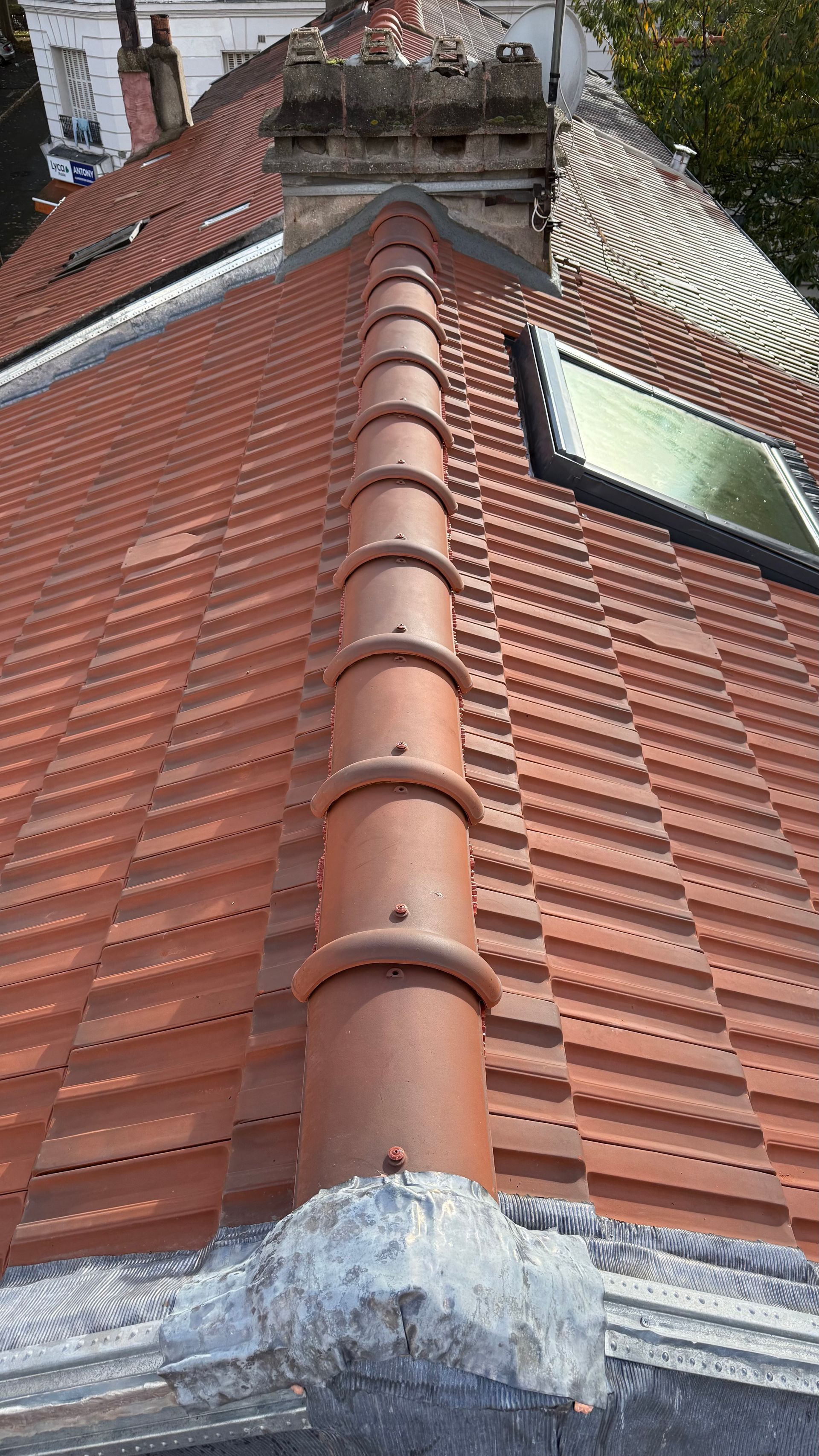 Toit de tuiles rouges orné d'une rangée de faîtières rondes en terre cuite. On aperçoit une lucarne.