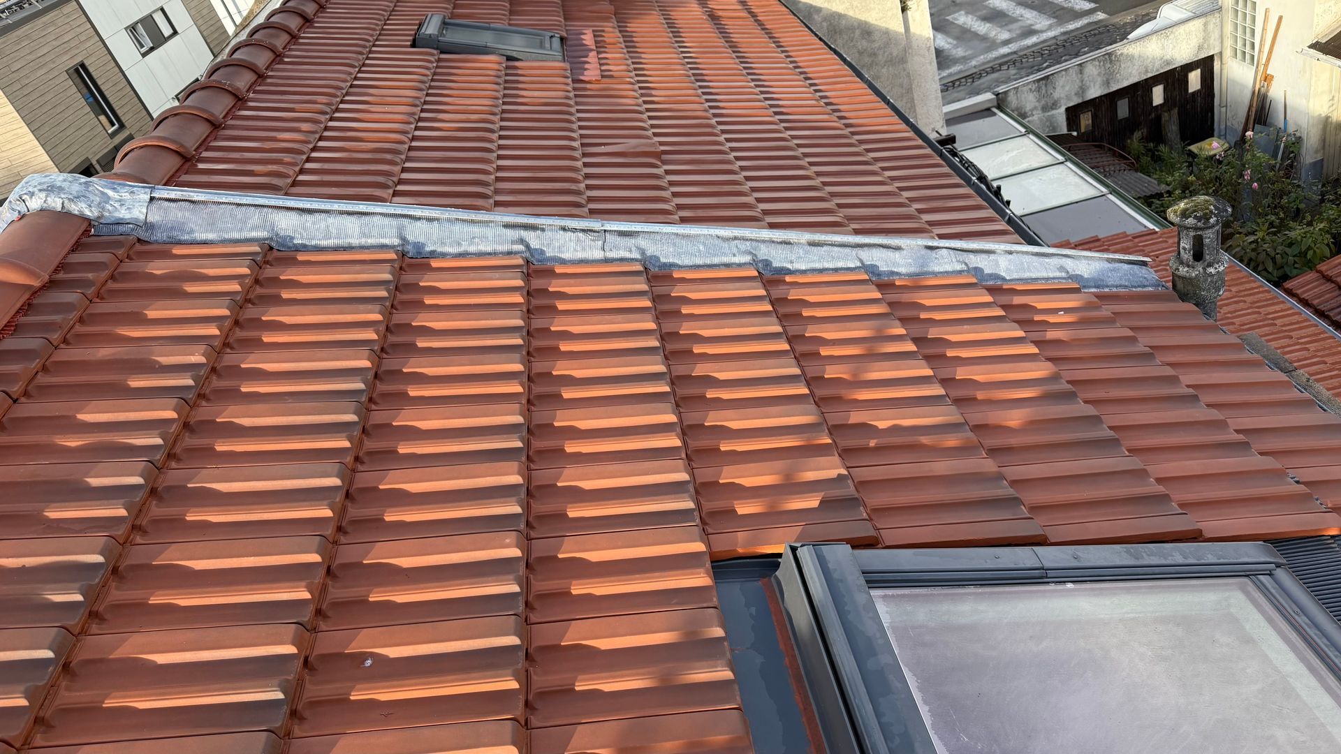 Toit en tuiles rouges avec un puits de lumière et une bande de solin métallique.