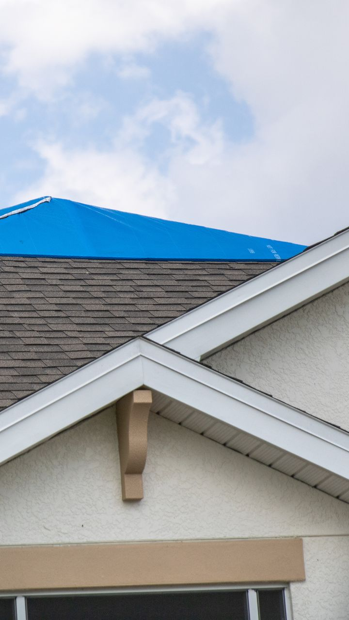 Toiture endommagée d'une maison recouverte d'une bâche bleue.
