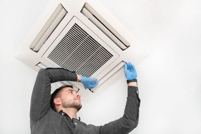 Un hombre que lleva guantes azules está trabajando en un aire acondicionado.