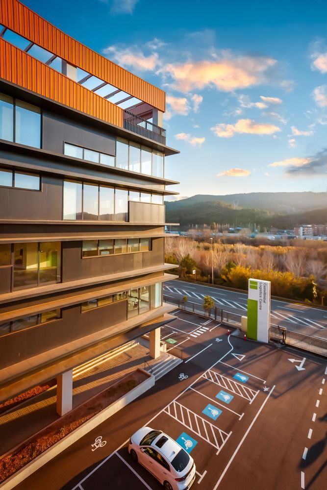 Edificio moderno con aparcamiento y estaciones de carga para vehículos eléctricos. Hay un coche aparcado. Montañas y cielo de fondo.