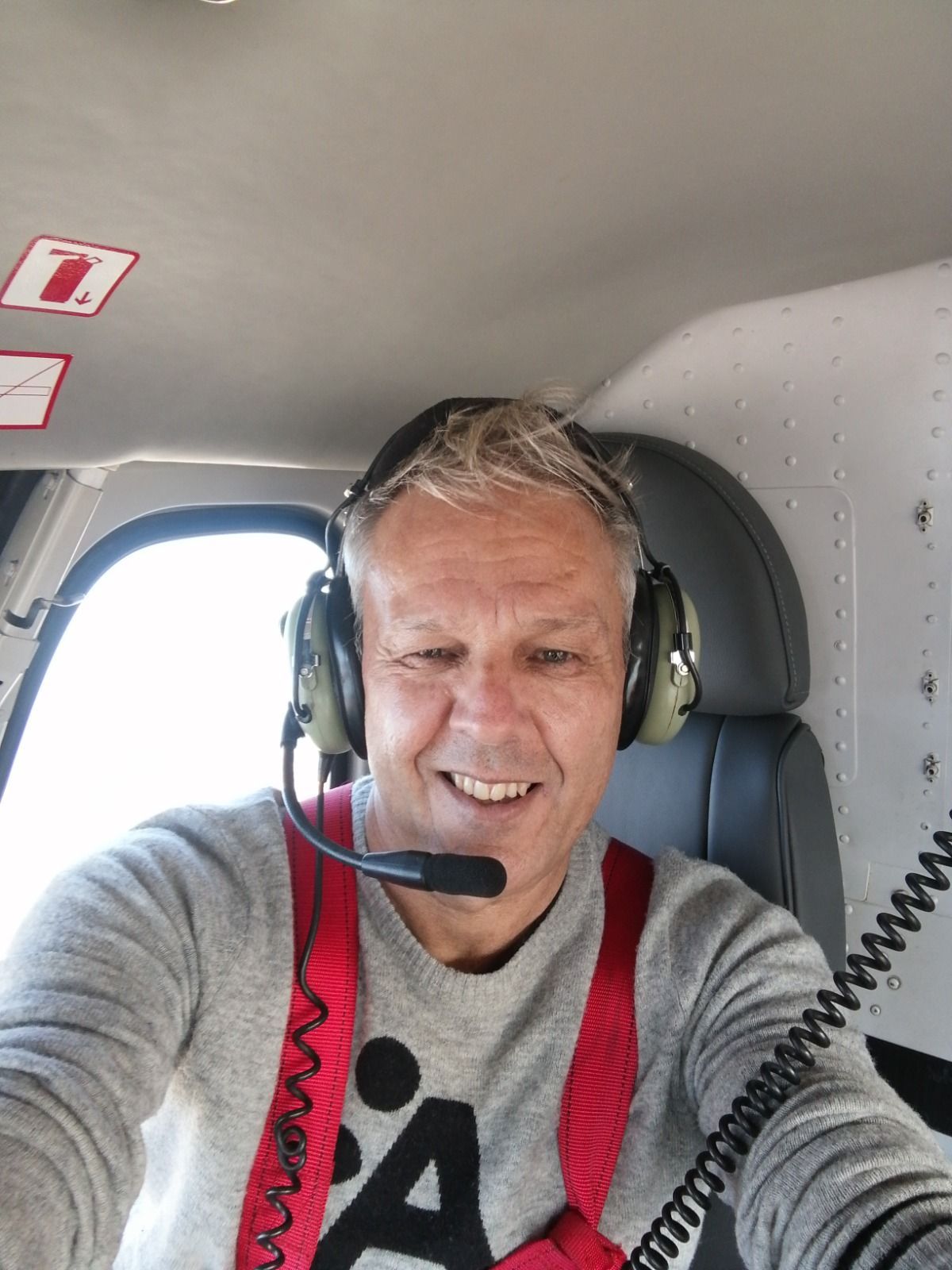 Hombre en la cabina de un helicóptero con auriculares y arnés, sonriendo a la cámara.