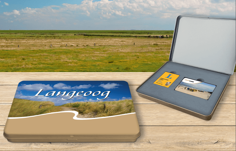 Geschenkset mit Strandmotiv „Langeoog“ auf einer Schachtel; offenes Etui mit Karten auf Holztisch vor Landschaftshintergrund.