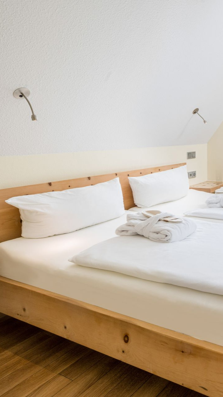 Schlafzimmer mit zwei Einzelbetten, weißer Bettwäsche, Holzrahmen, kleinem Fenster, braunen Vorhängen und einem Fernseher.