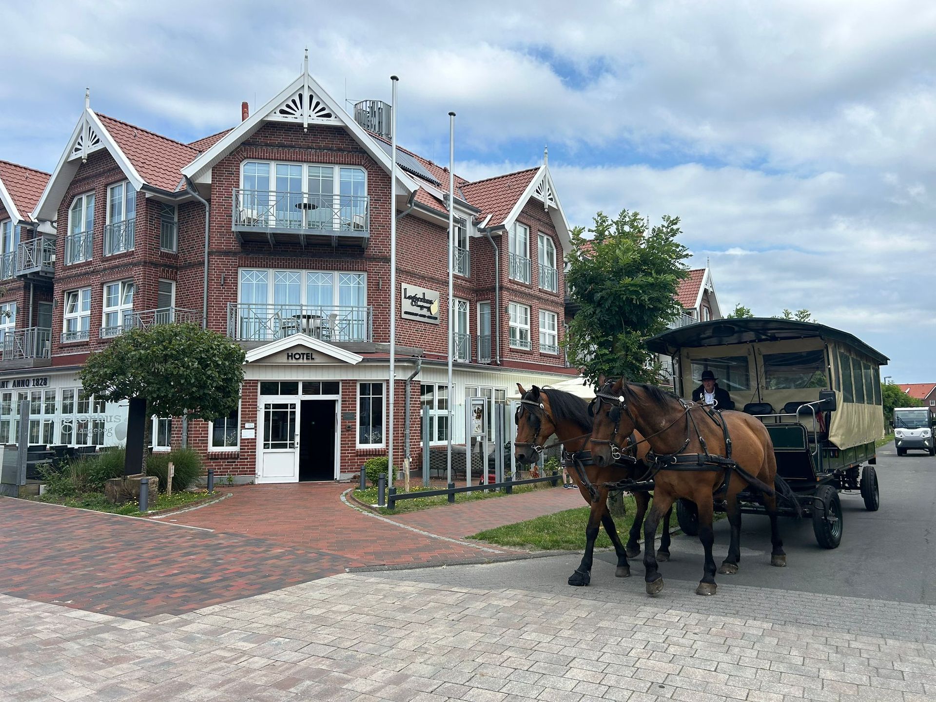Hotel aus rotem Backstein mit weißen Verzierungen, rotem Dach und Balkonen in Küstenlage.