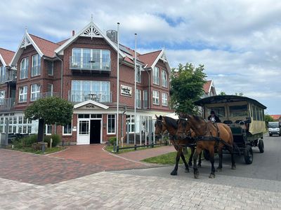 Hotel aus rotem Backstein mit weißen Verzierungen, rotem Dach und Balkonen in Küstenlage.