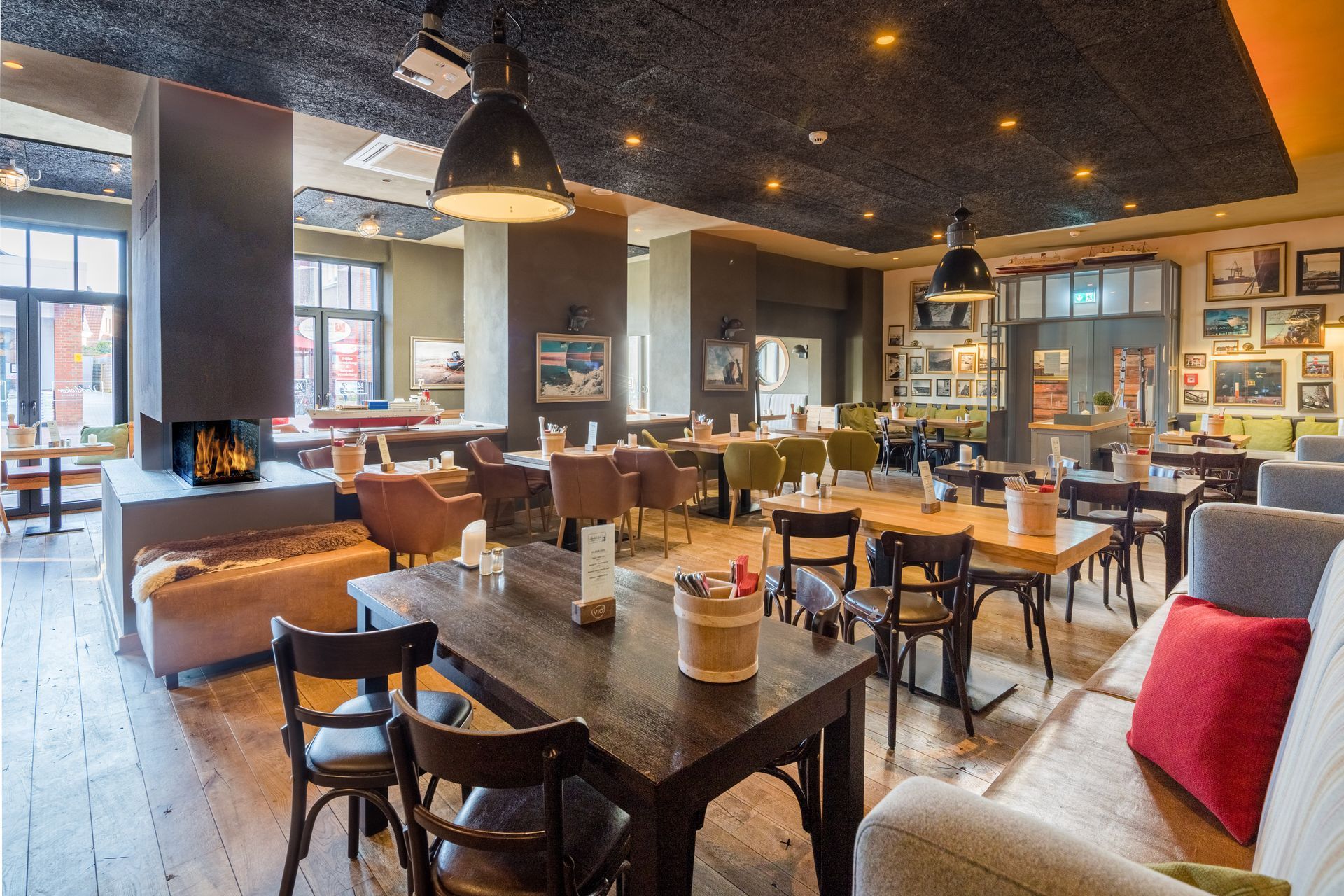 Innenansicht eines Restaurants mit Tischen, Stühlen, Kamin und gedämpftem Licht.