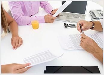 Personas revisando documentos en una mesa blanca con una computadora portátil, una calculadora y un vaso de jugo.