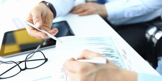 Tres personas de traje en una mesa revisando documentos, al fondo hay un mazo y una balanza de la justicia.