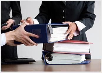 Personas intercambiando carpetas llenas de documentos, apilados en un escritorio.