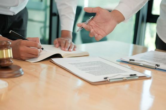 Dos personas en un entorno legal, firmando documentos en un escritorio; mazo al costado.