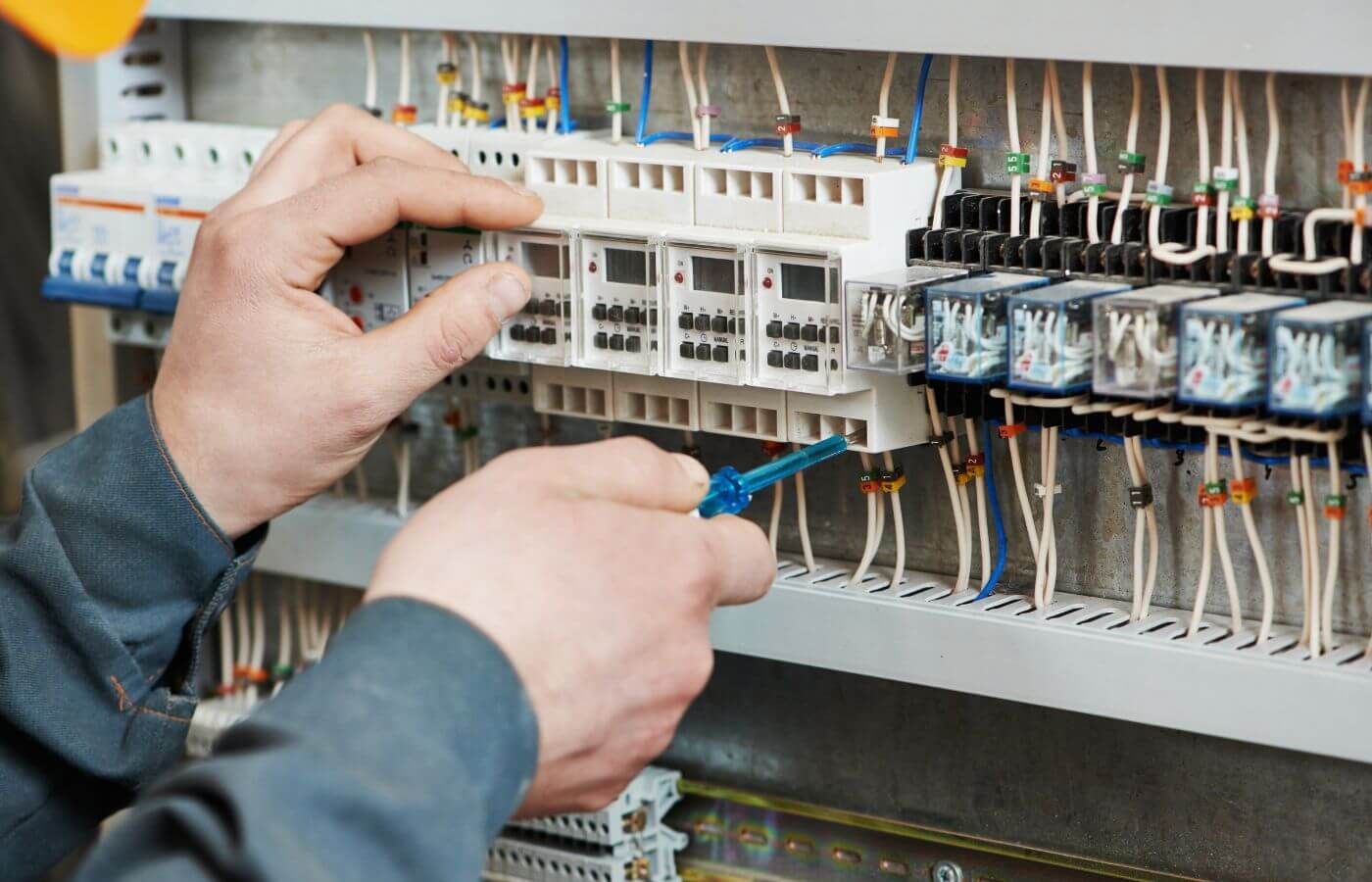 Mains d'un homme travaillant sur la connectique d'un tableau électrique.