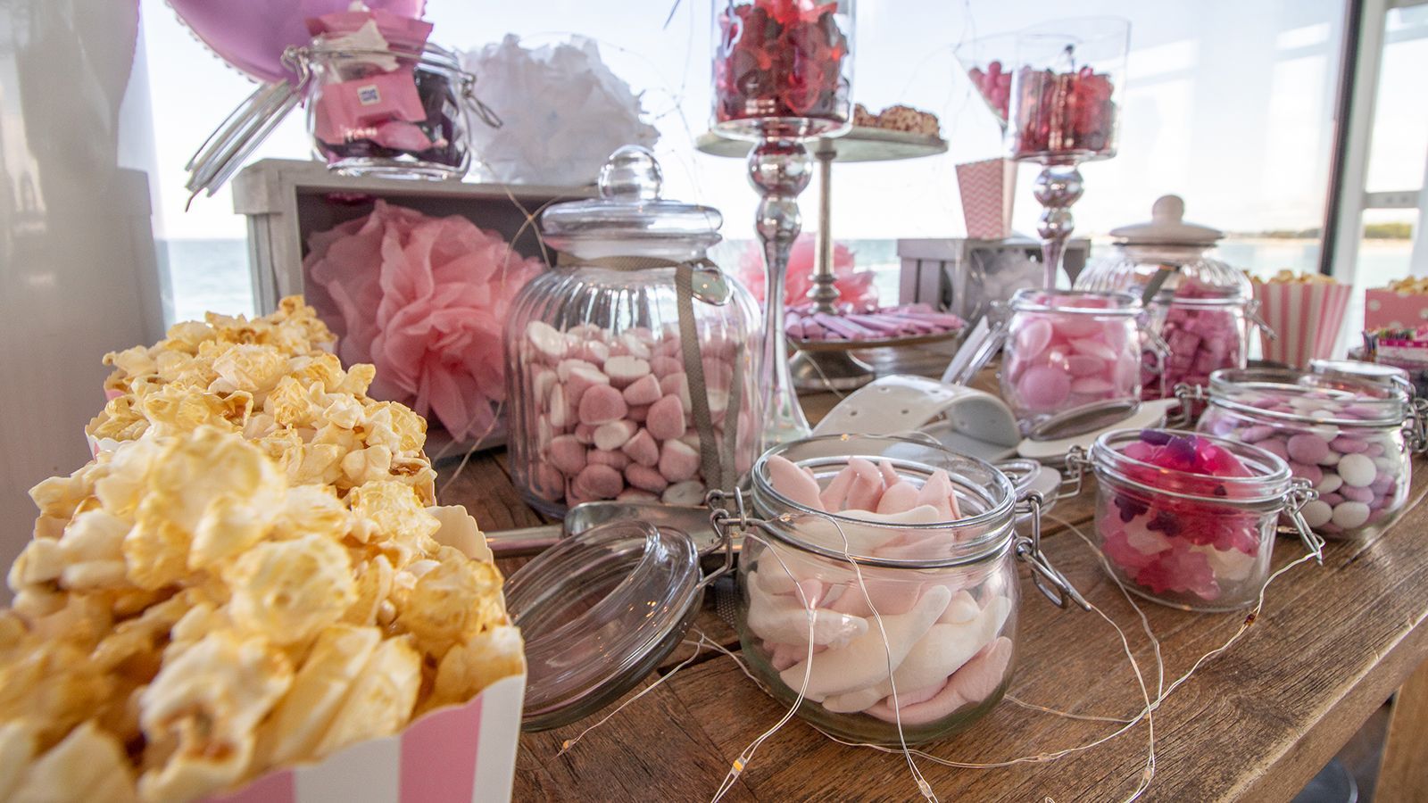 Süßigkeiten- und Snackbuffet mit rosa und weißen Süßigkeiten im Glas und Popcorn.