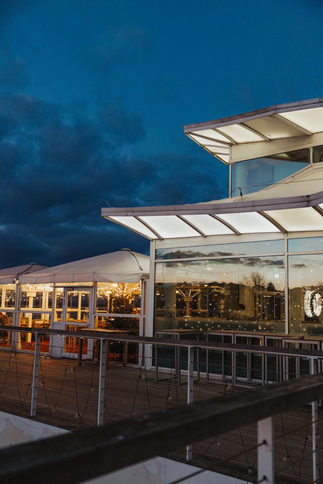 Modernes Gebäude mit großen Fenstern und Markisen in der Abenddämmerung unter einem dunklen, bewölkten Himmel.