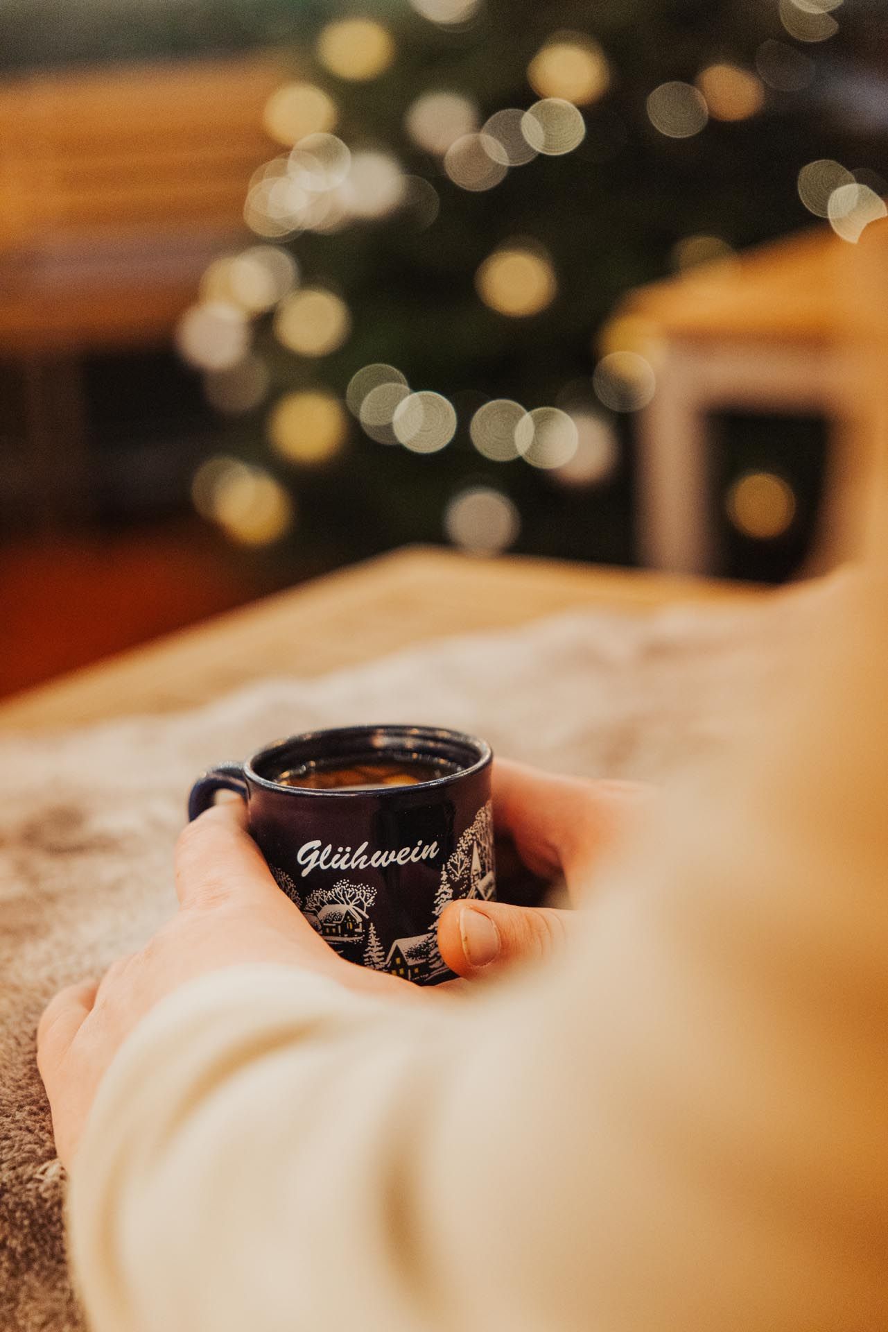 Eine Person hält einen kleinen blauen Becher Glühwein vor einem Weihnachtsbaum mit Bokeh-Lichtern.