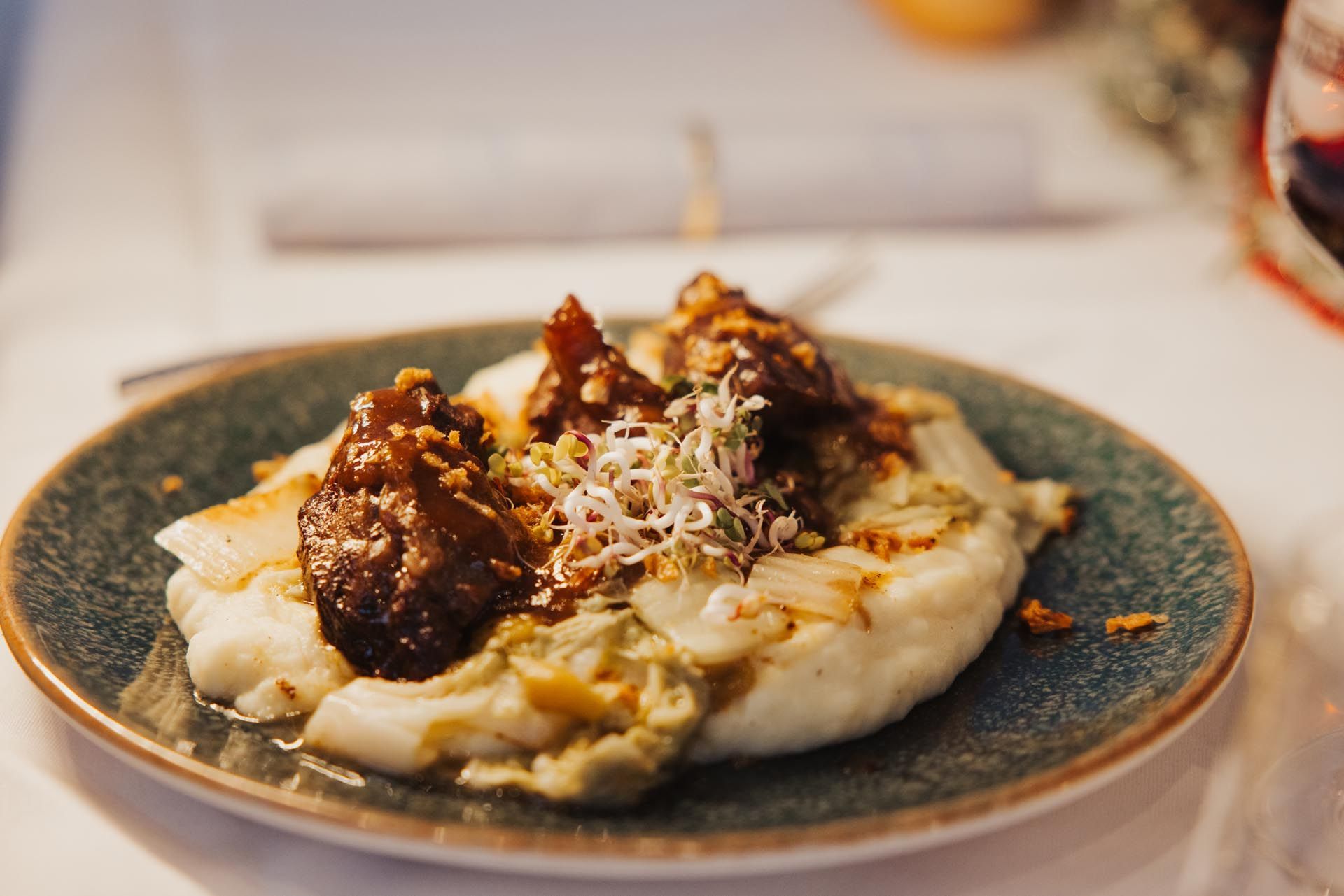 Tellergericht: Weißes und grünes Kartoffelpüree mit dunkler Soße und Sprossen auf einem türkisfarbenen Tellerrand.