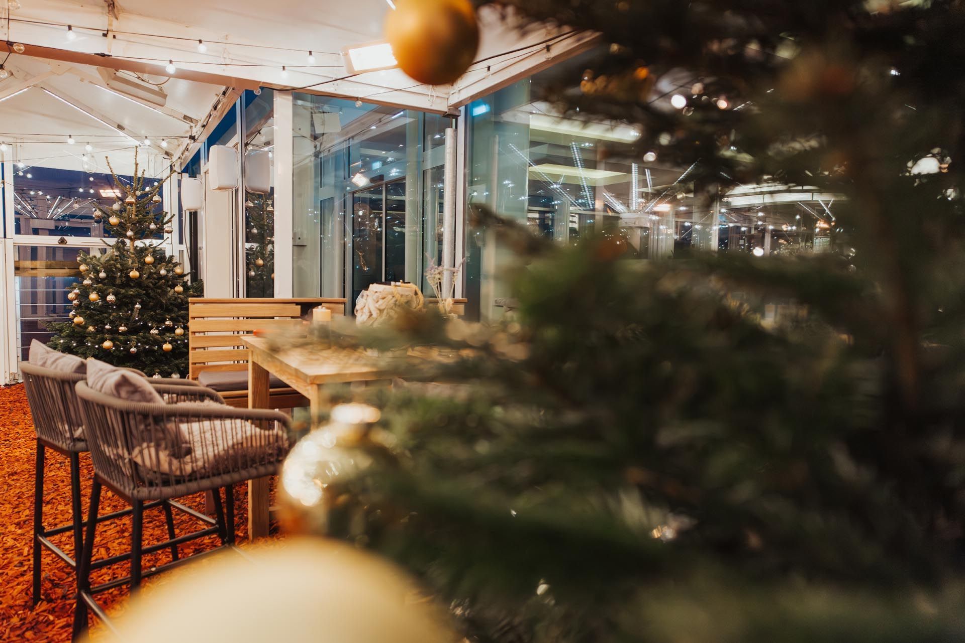 Gemütliche Weihnachtsszene im Freien mit geschmücktem Baum, Sitzgelegenheiten und Lichterketten.