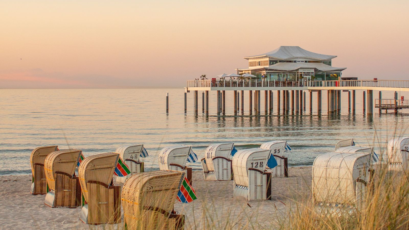 Strandstühle mit Blick auf einen Pavillon am Pier über ruhigem Wasser bei Sonnenuntergang