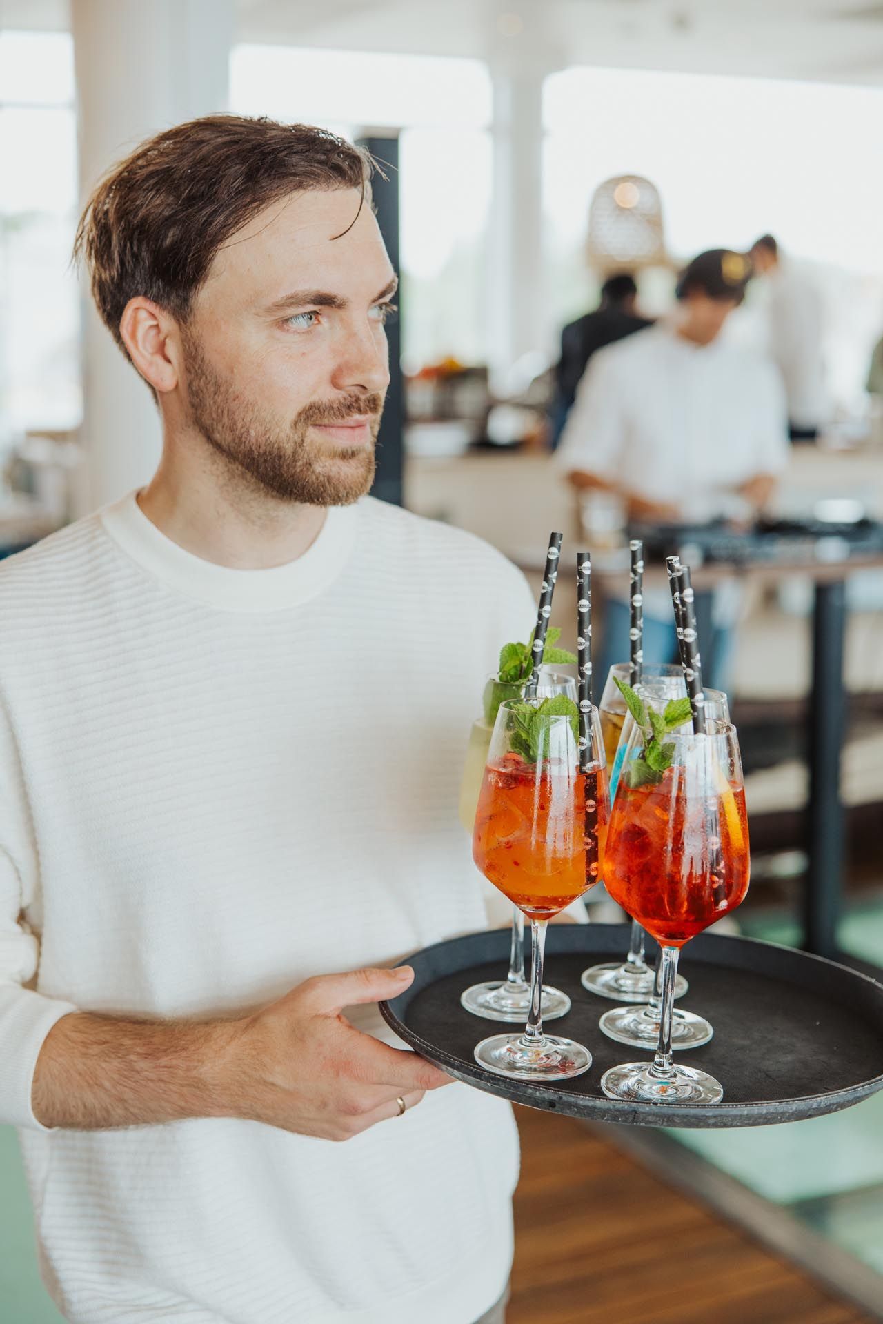 Mann hält Tablett mit Cocktails in einem hellen Restaurant.