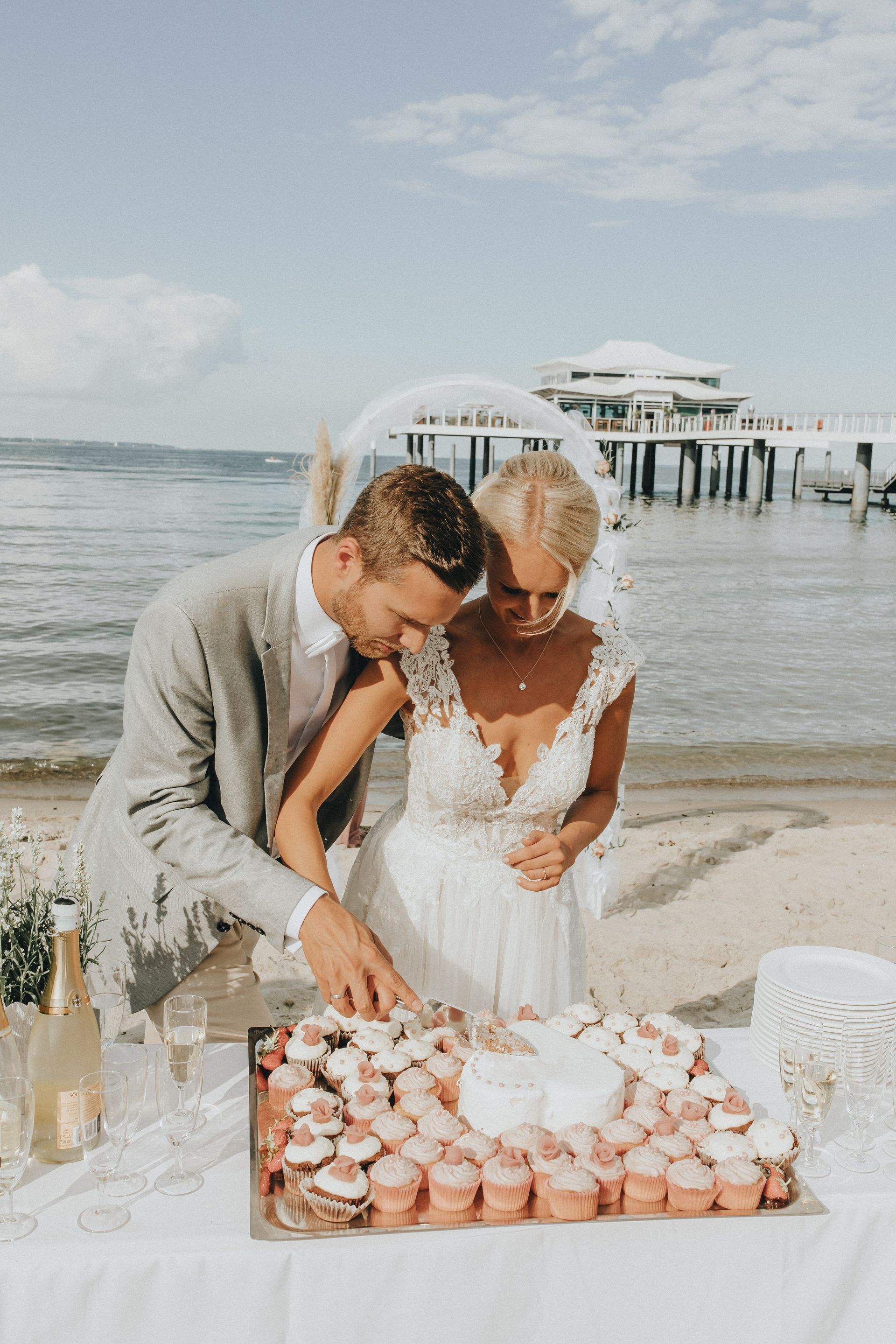 Hochzeitspaar schneidet die Hochzeitstorte am Strand bei einem Empfang an einer Seebrücke an