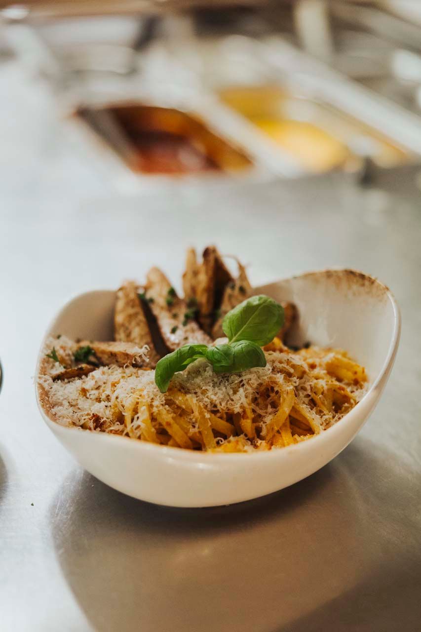 Nudelgericht in einer weißen Schüssel, garniert mit Basilikum und Parmesan, dazu Hähnchenscheiben.