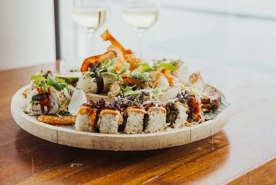 Sushi-Platte mit zwei Gläsern Weißwein auf einem Holztisch.