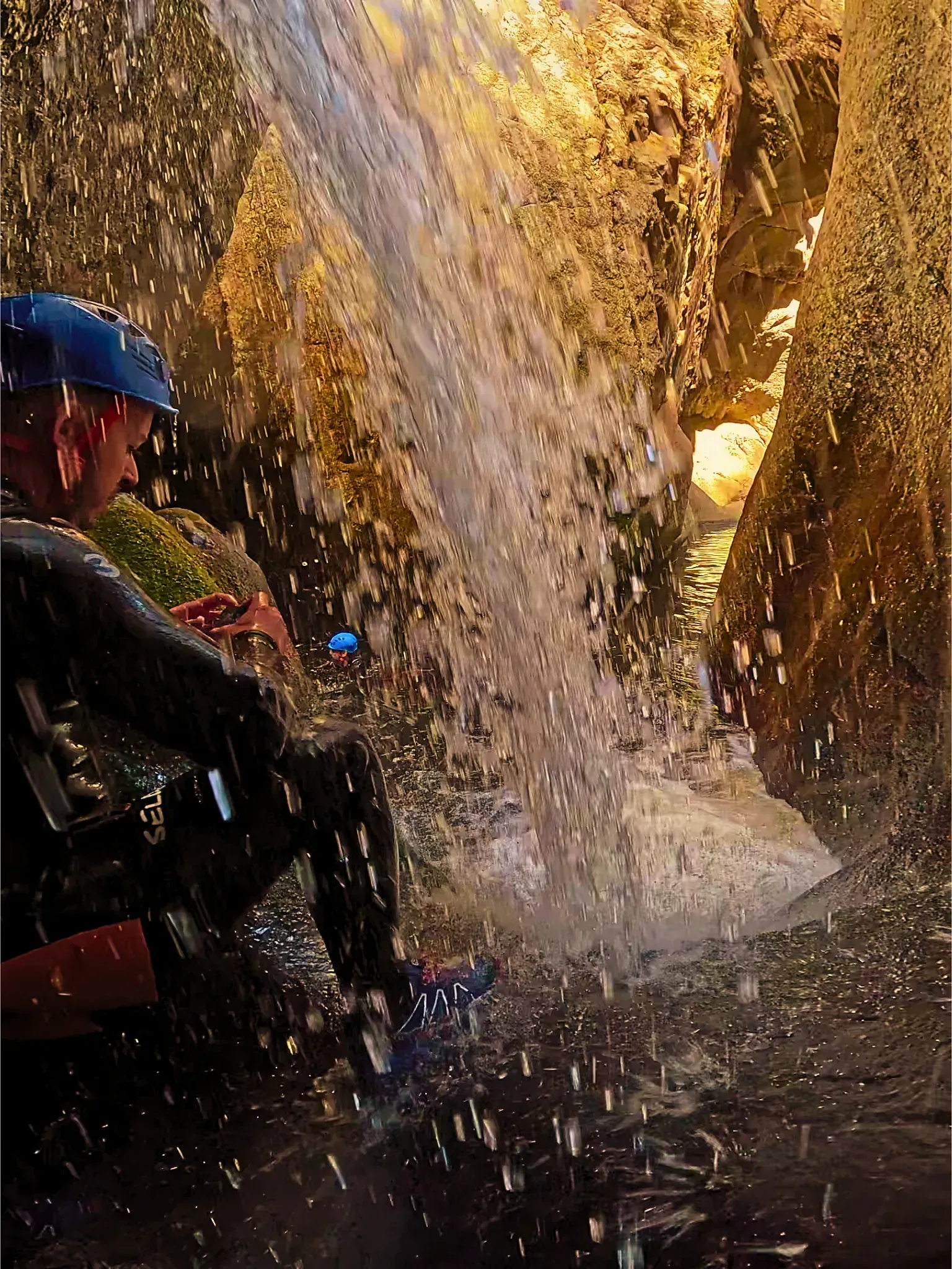 Un hombre está sentado frente a una cascada en una cueva.