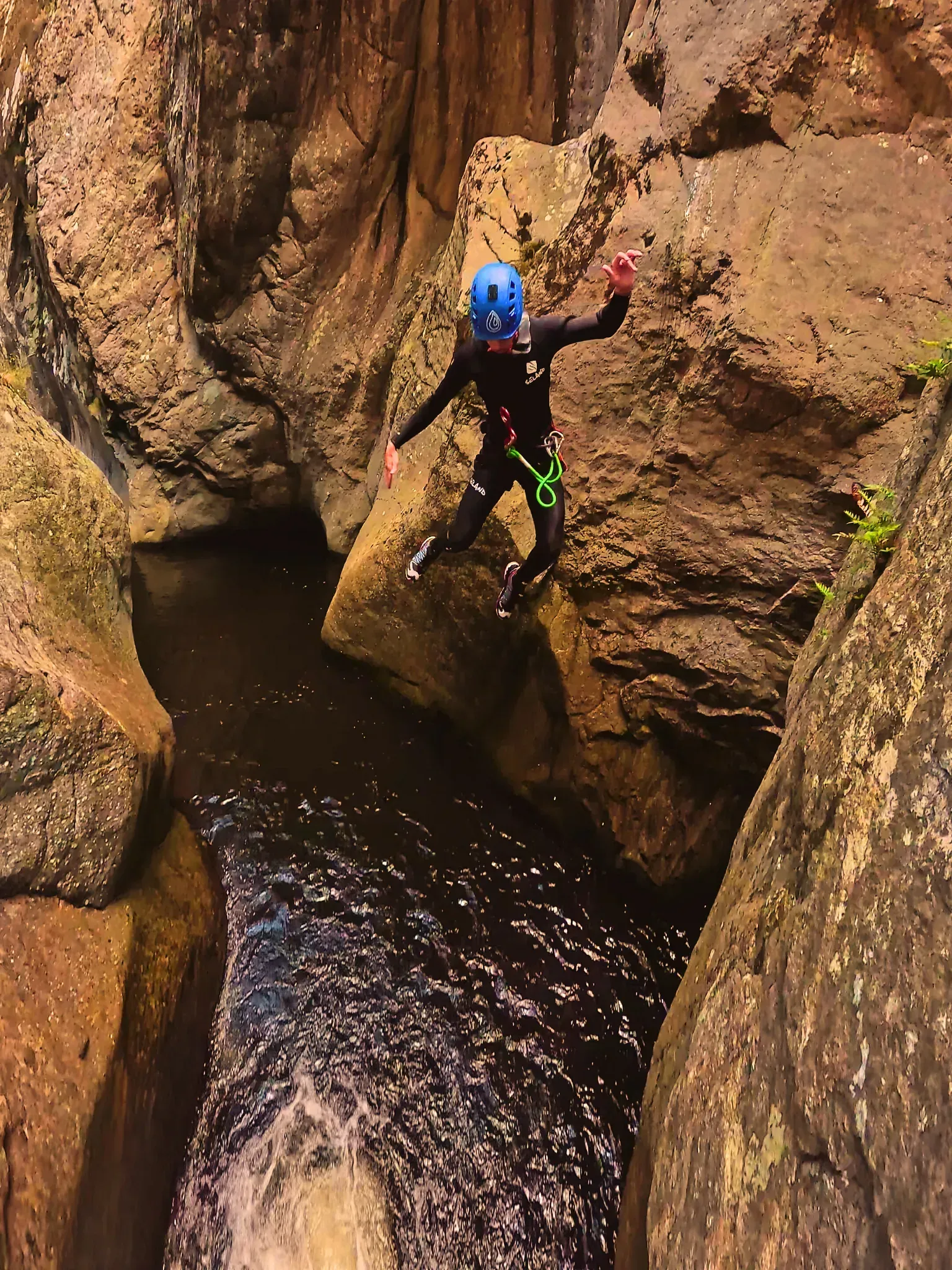Una persona está saltando a un río entre dos rocas.