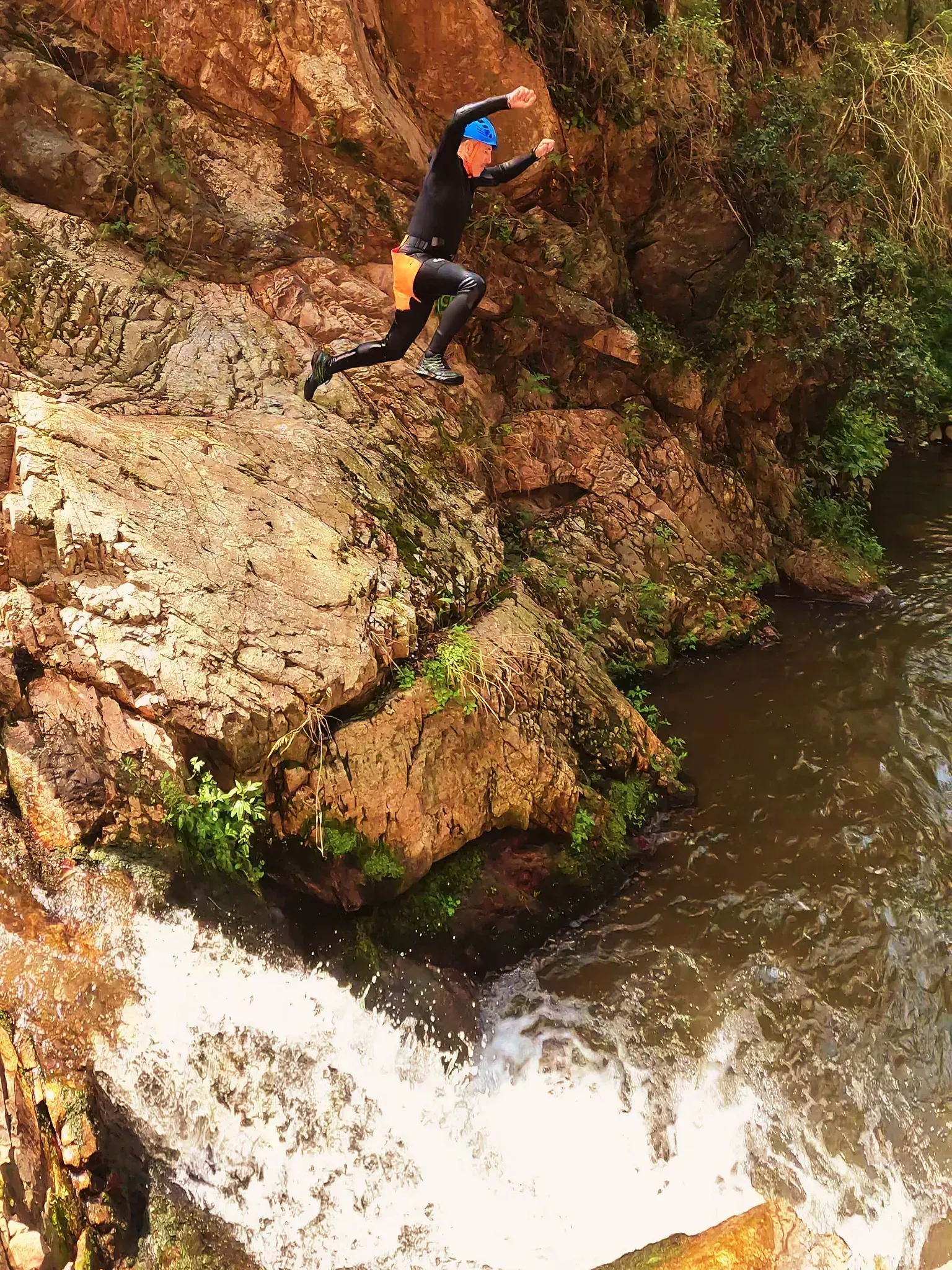 Un hombre está saltando desde un acantilado a un río.