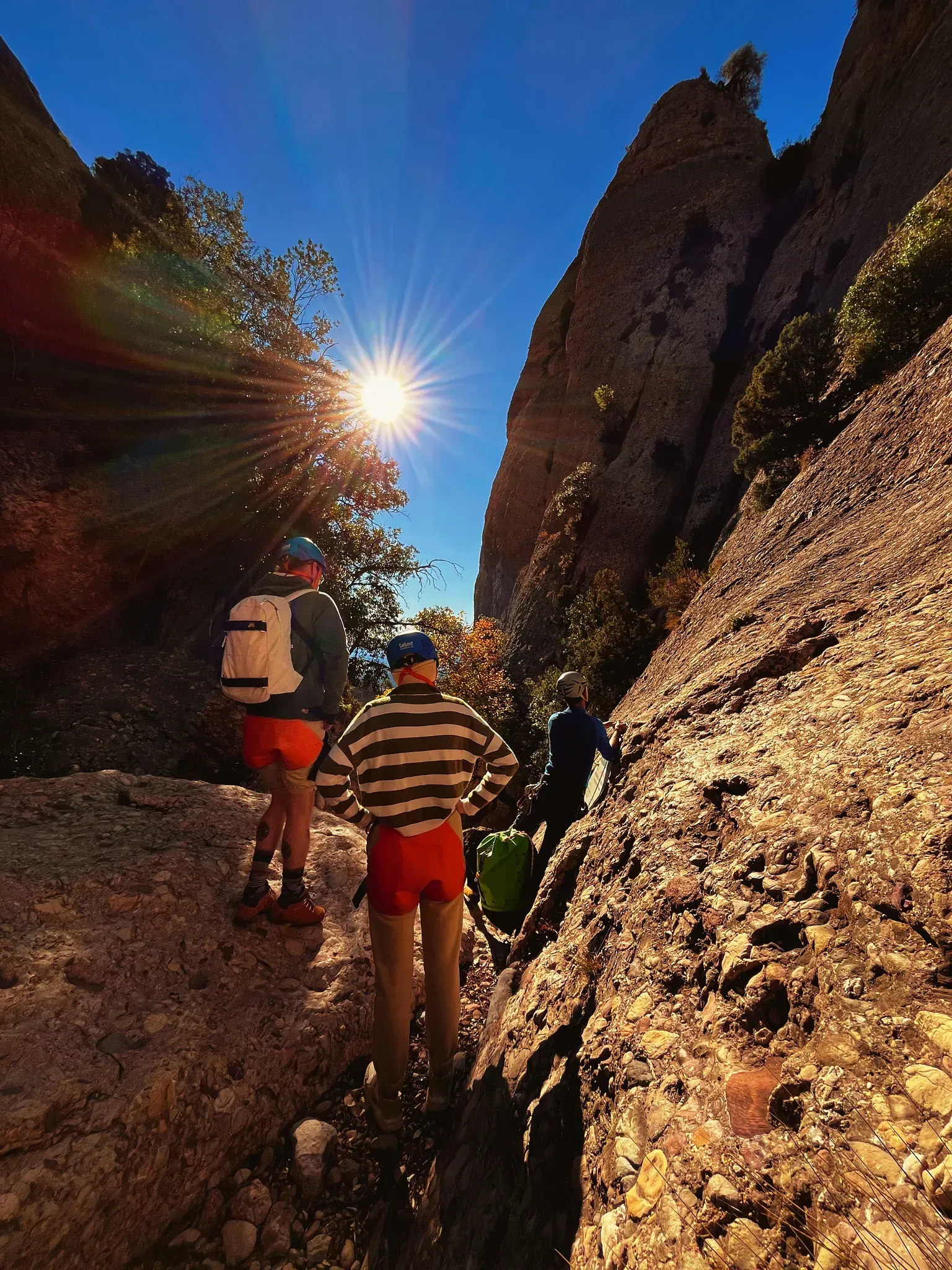 Dos personas caminando por un sendero rocoso con el sol brillando a través de los árboles.
