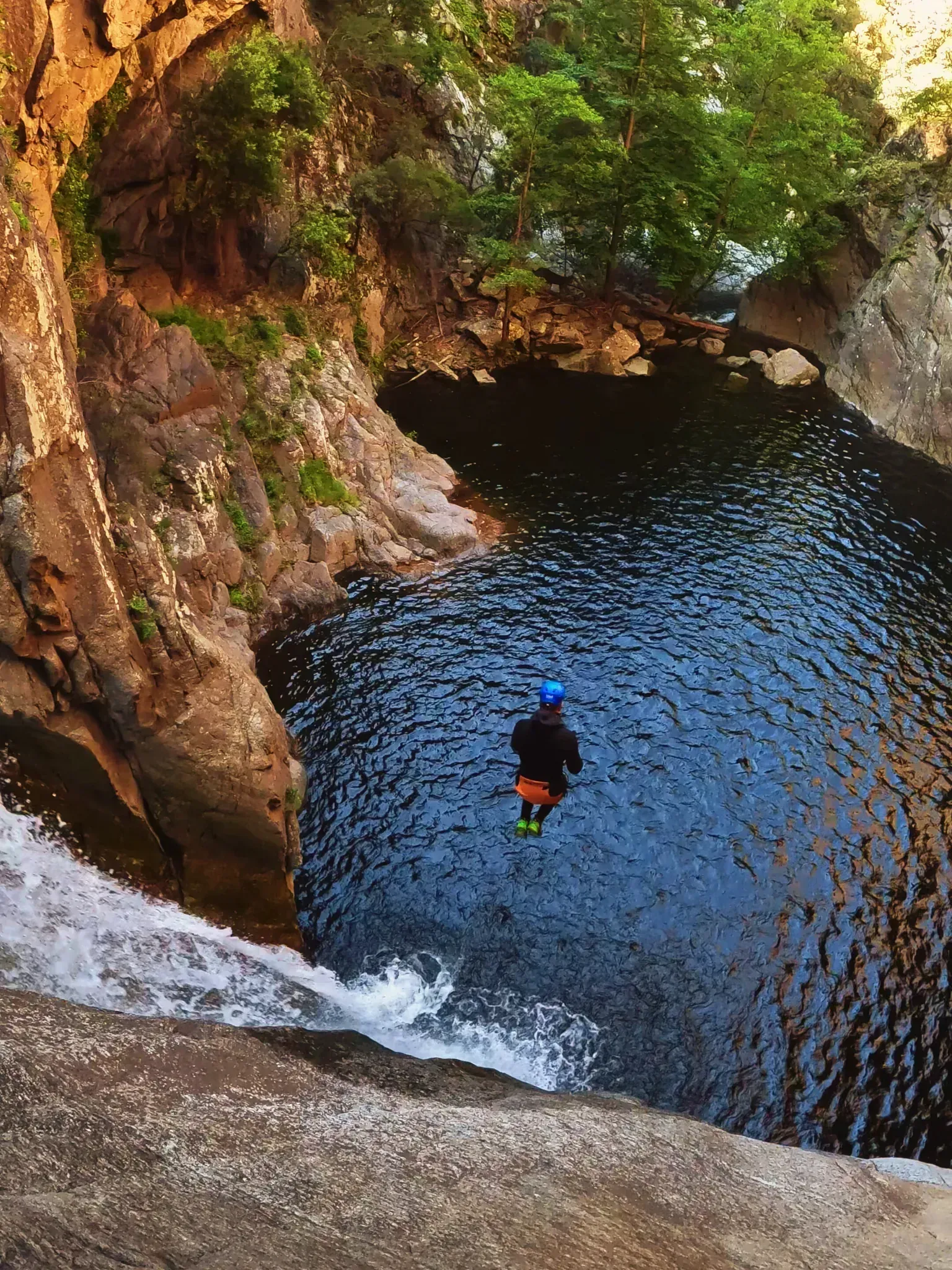 Una persona está nadando en un río al lado de una cascada.