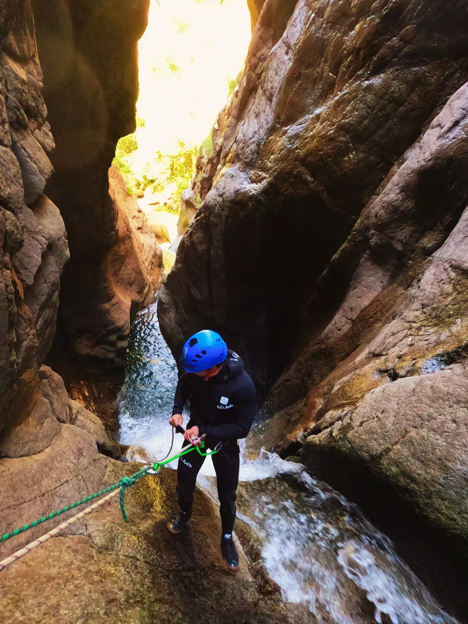 Un hombre con un casco azul está escalando una cascada en un cañón.