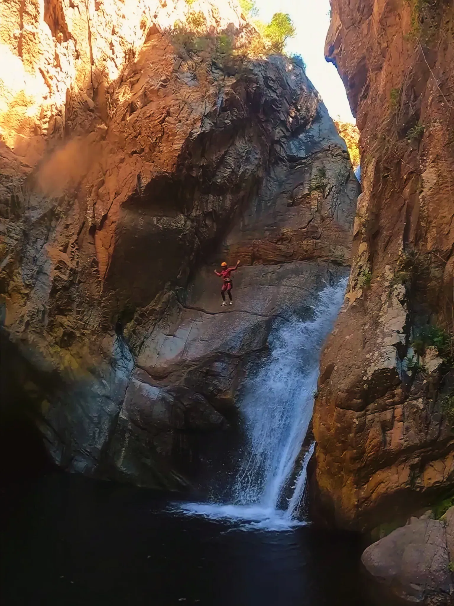 Una persona está parada frente a una cascada en un cañón.