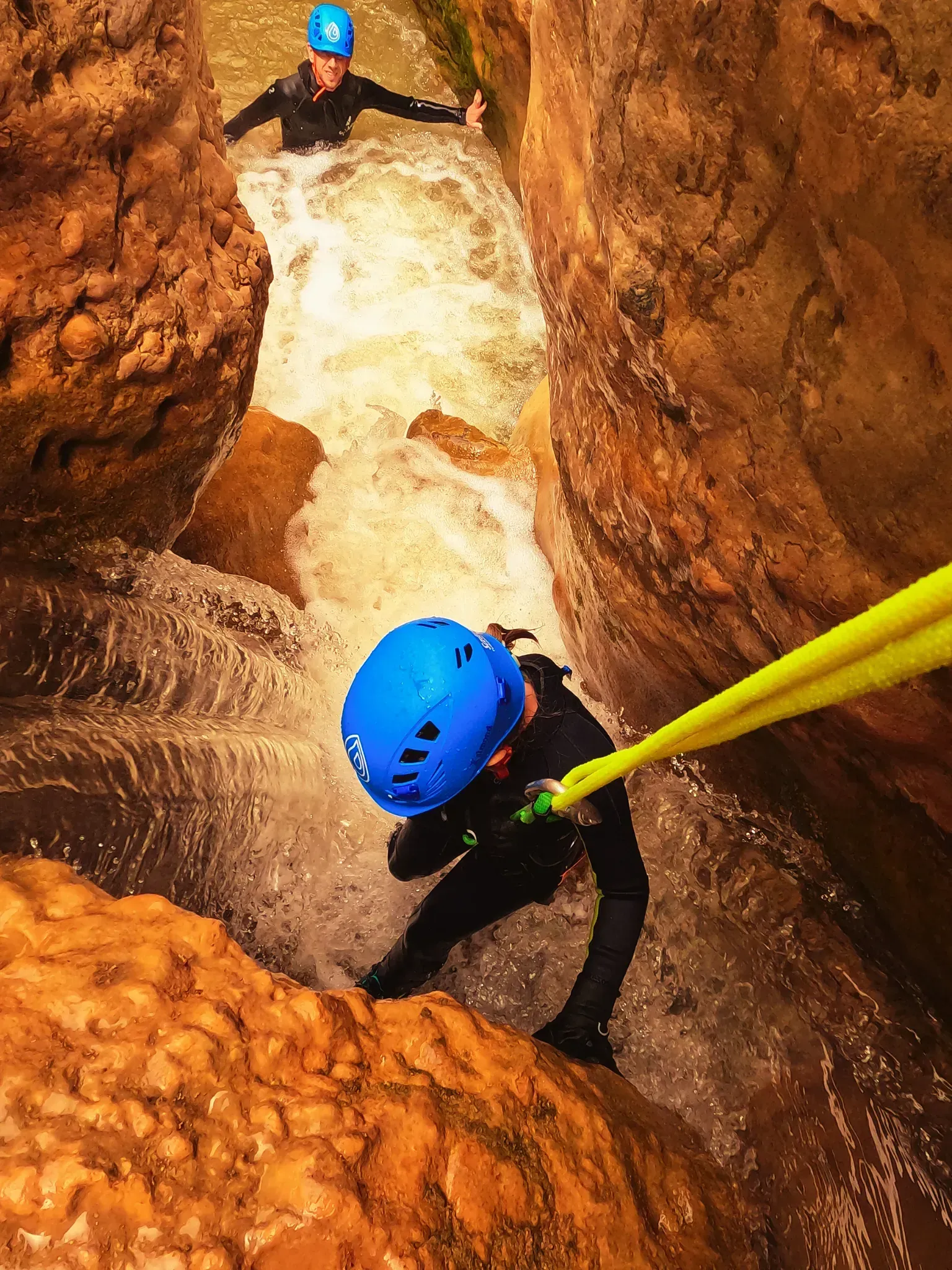 Un hombre con un casco azul baja por una cascada.