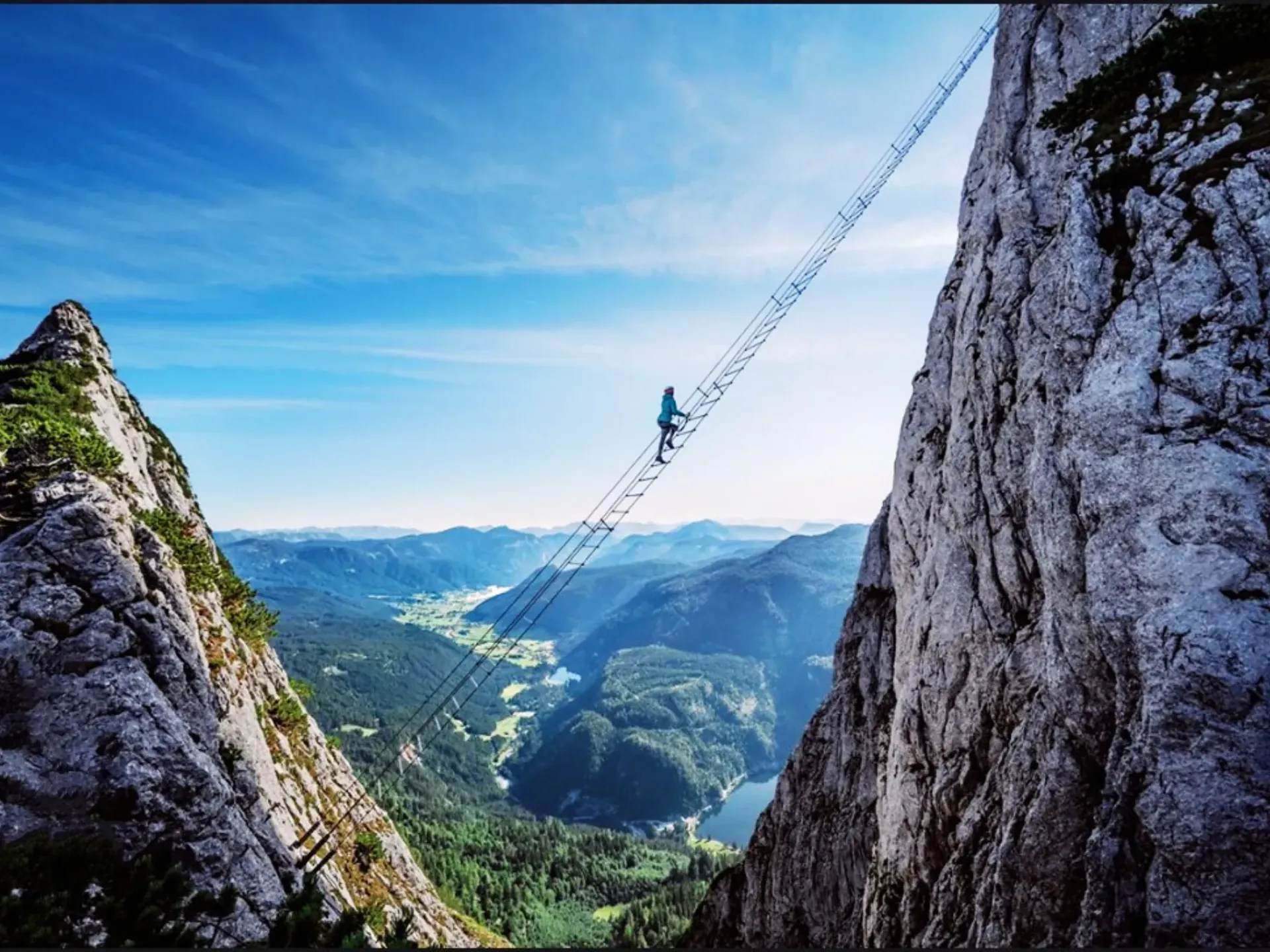 Una persona camina por un puente colgante entre dos montañas.