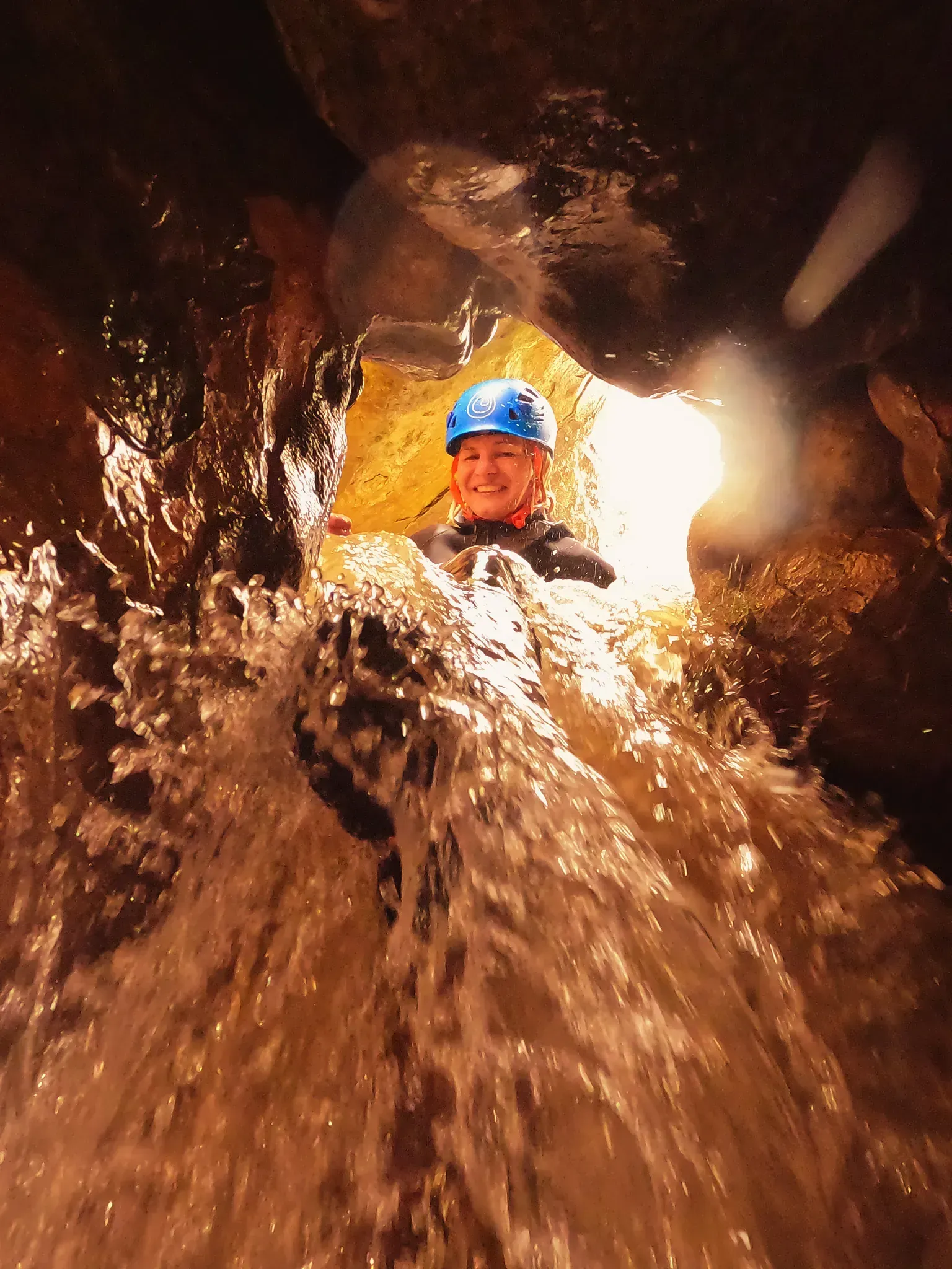 Un hombre con casco azul baja por una cascada.