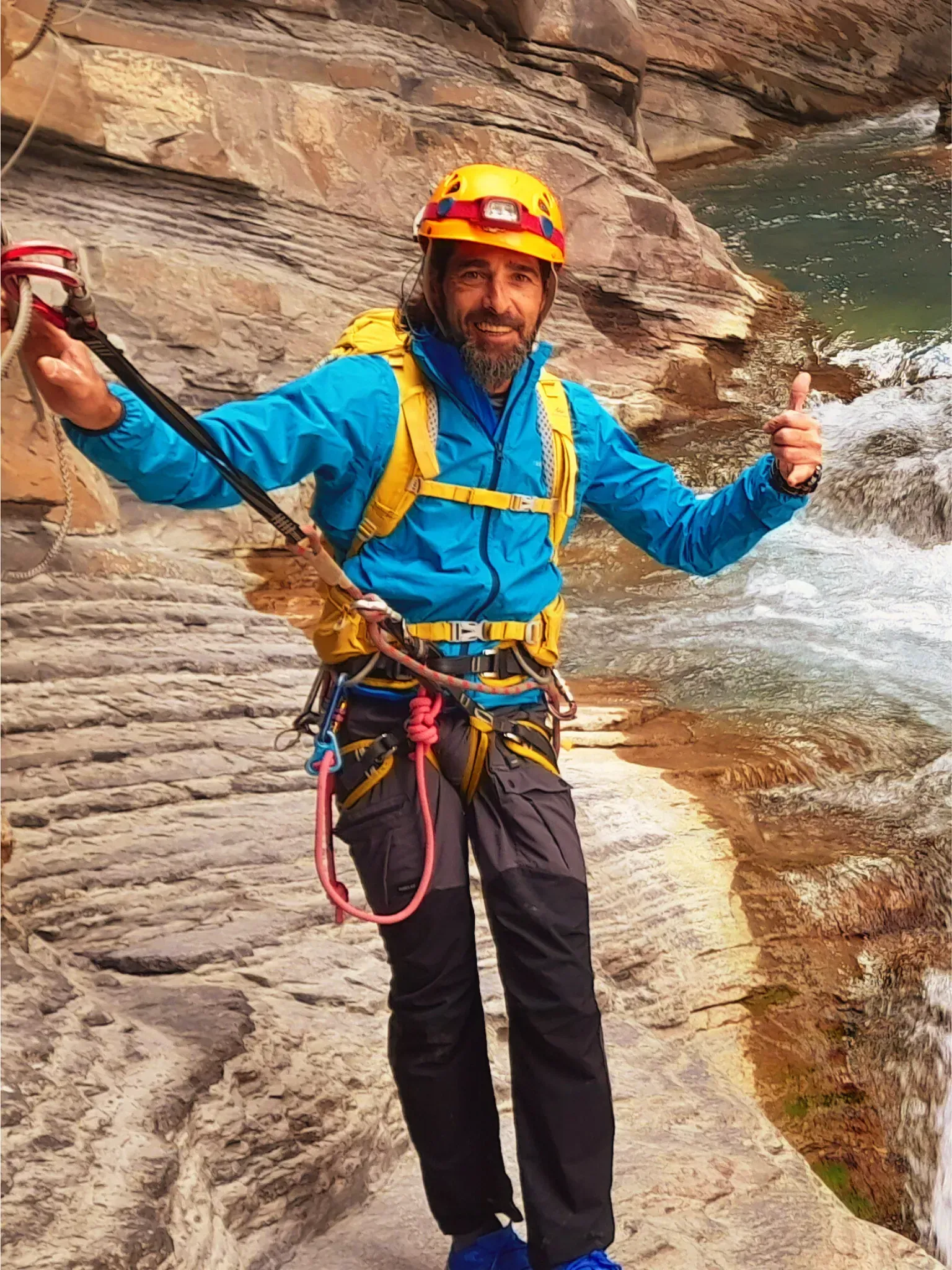 Un hombre que lleva un casco y hace un gesto de aprobación con el pulgar está parado al lado de un río.
