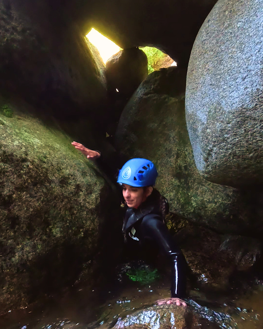 Una persona con traje de neopreno y casco azul sube por un estrecho paso de roca con una abertura para la luz.