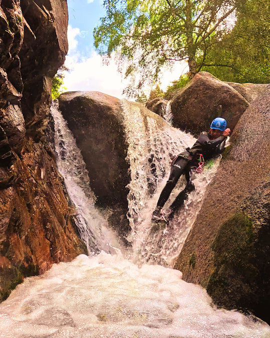 Persona descendiendo en rápel por una cascada entre paredes de roca, con casco y traje de neopreno.