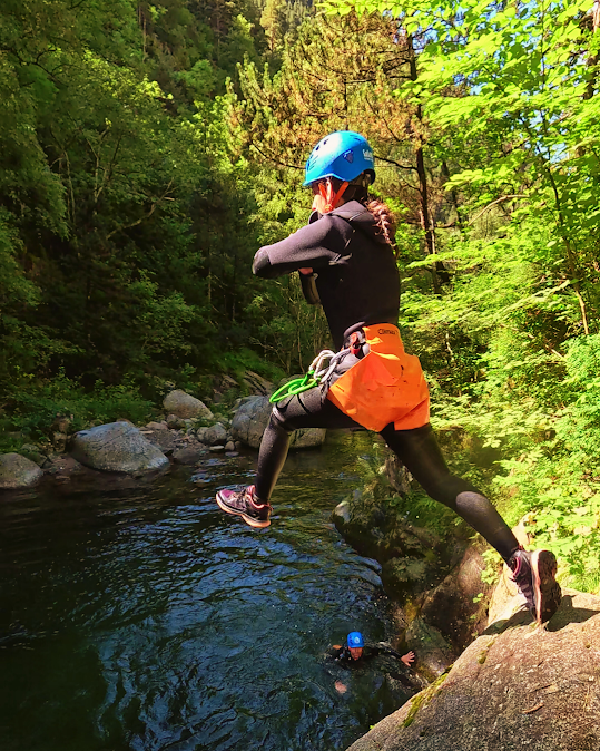 Persona con traje de neopreno saltando a un río rodeado de un exuberante bosque verde.