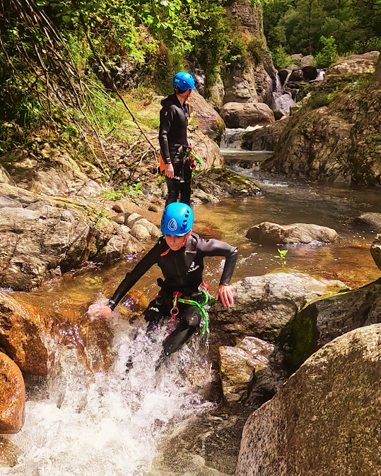 Dos personas con trajes de neopreno y cascos haciendo barranquismo en un arroyo rocoso.